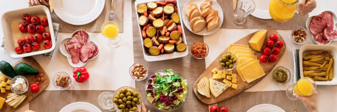 Overhead view of a lively brunch setup with assorted foods, cheeses, and juices on a table.