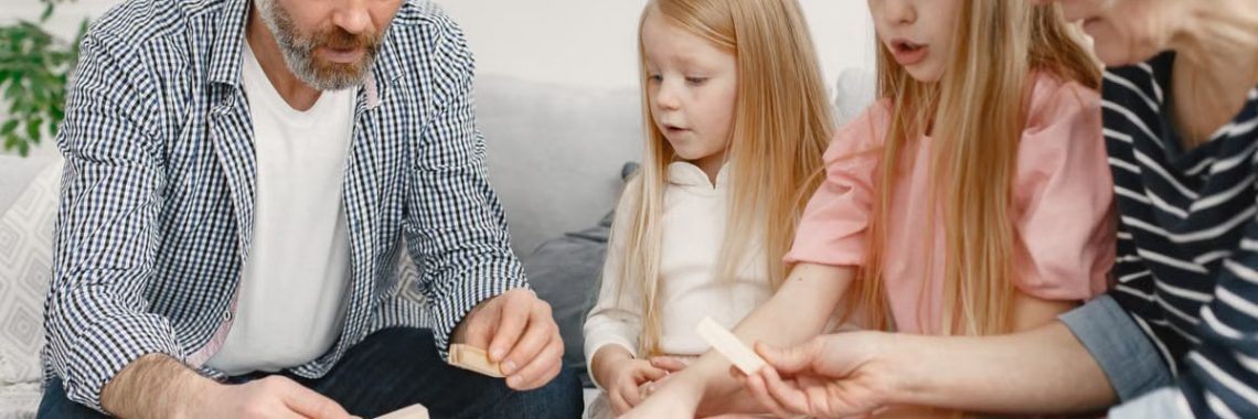 Four family members of different ages engage with toy blocks on a table indoors.