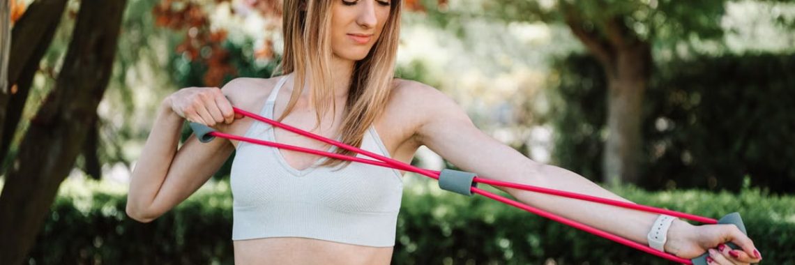 Fit woman using a resistance band for exercise in a sunny outdoor setting.